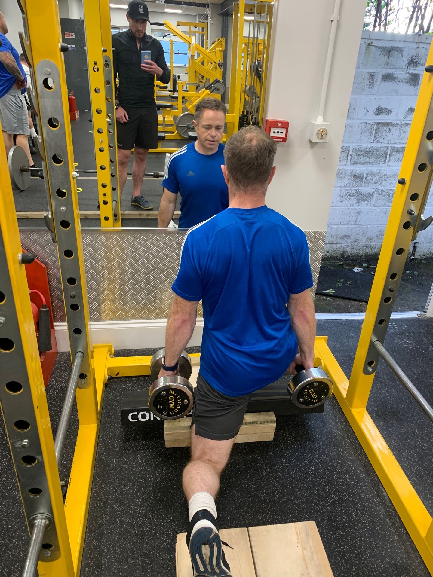 Client doing a weighted split squat with trainer standing behind supervising technique 